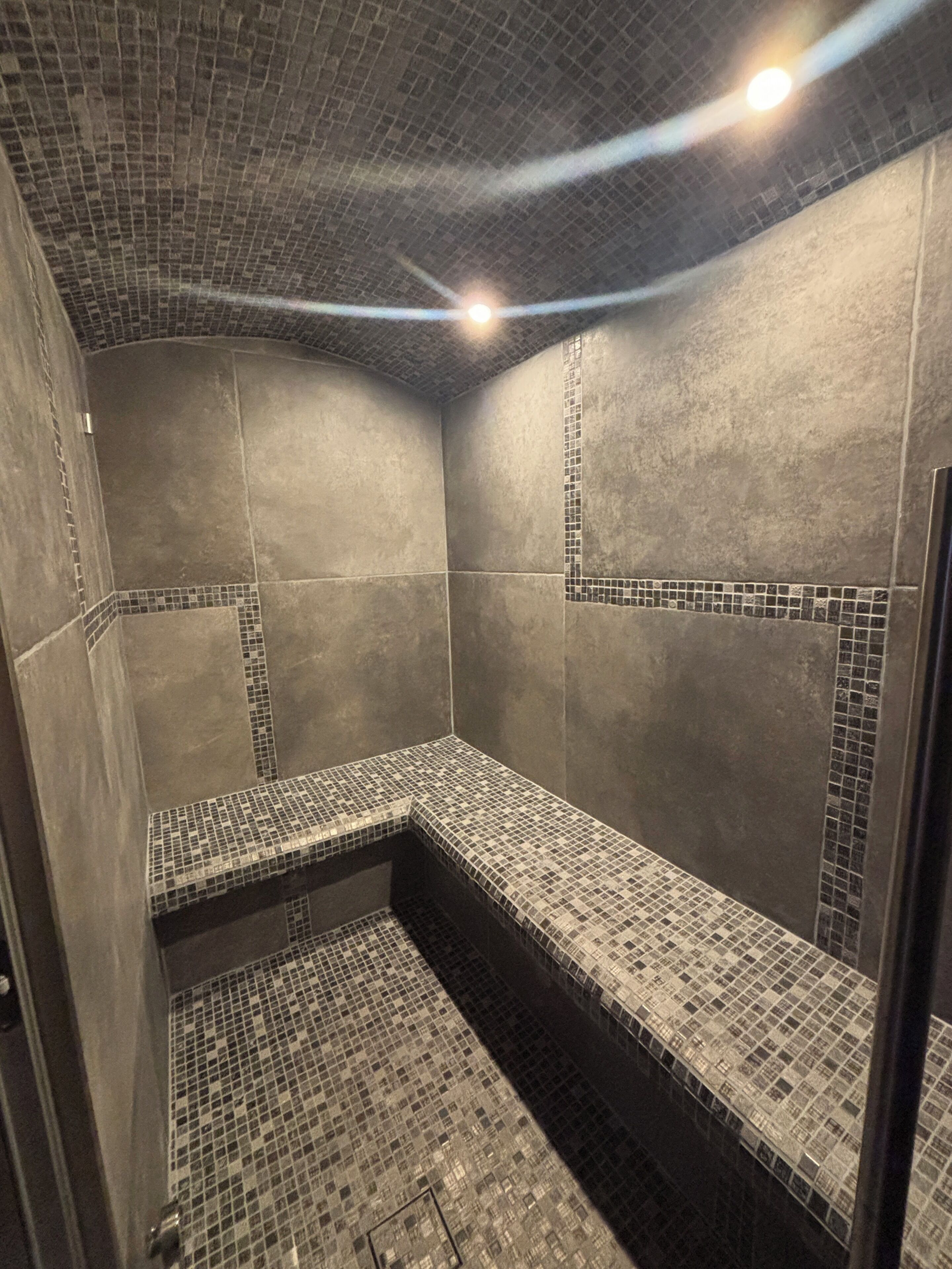 Eine geflieste Dusche mit Sitzbank, ein gefliester Boden und eine Decke mit Rastermuster.