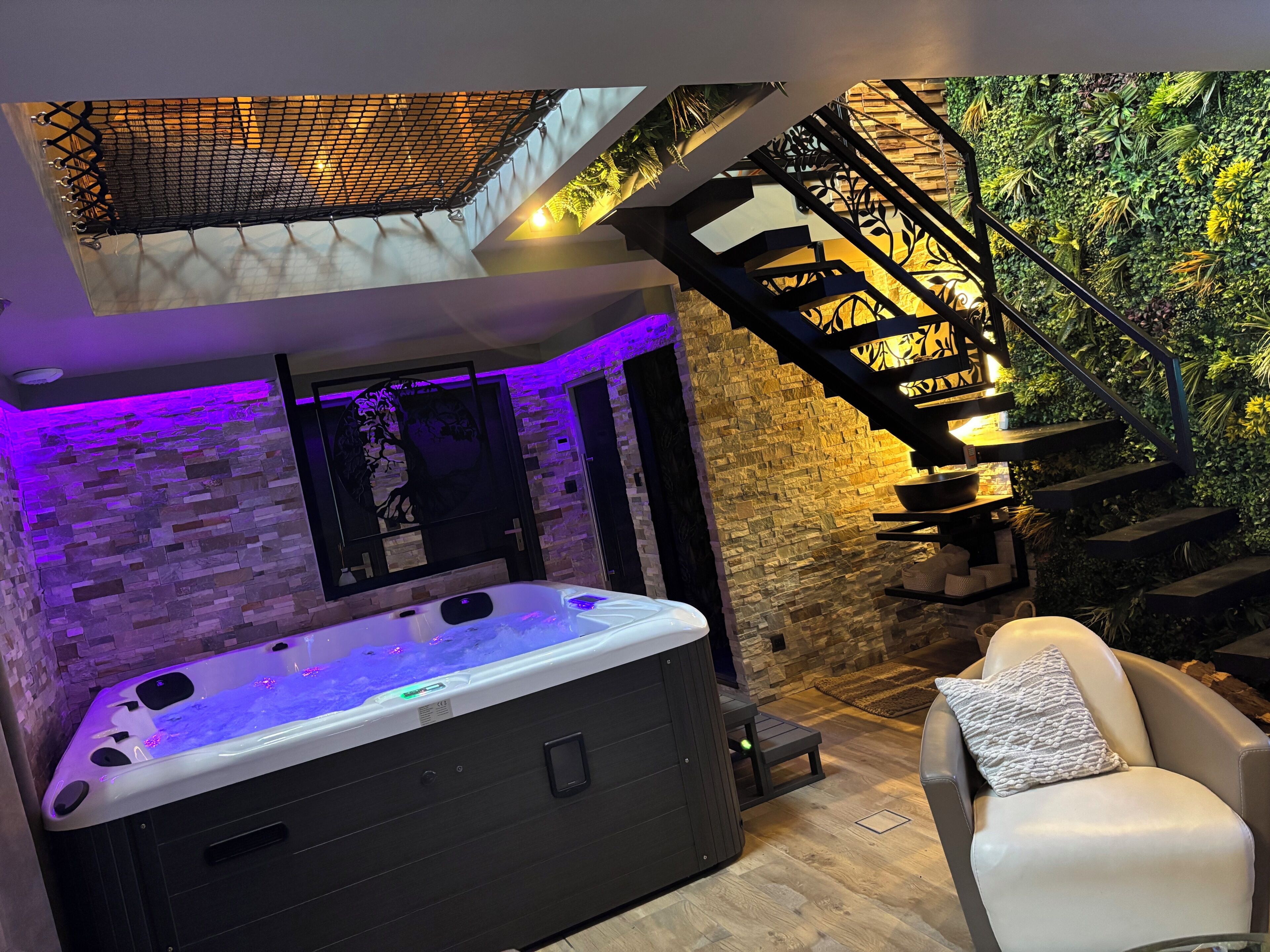 A modern spa area with a hot tub, a staircase with a green wall, and a stone wall.