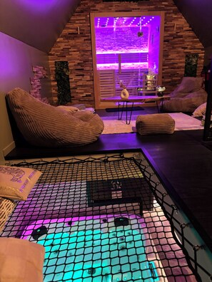 Um quarto aconchegante com teto inclinado, uma poltrona de saco, uma mesa pequena com um vaso, e uma área com mosquiteiro em primeiro plano.