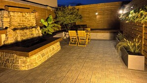 An outdoor patio area with a stone wall, wooden seating, and a small water feature. - Cozy 1-bedroom house in fantastic Rosult with AC (Rosult)