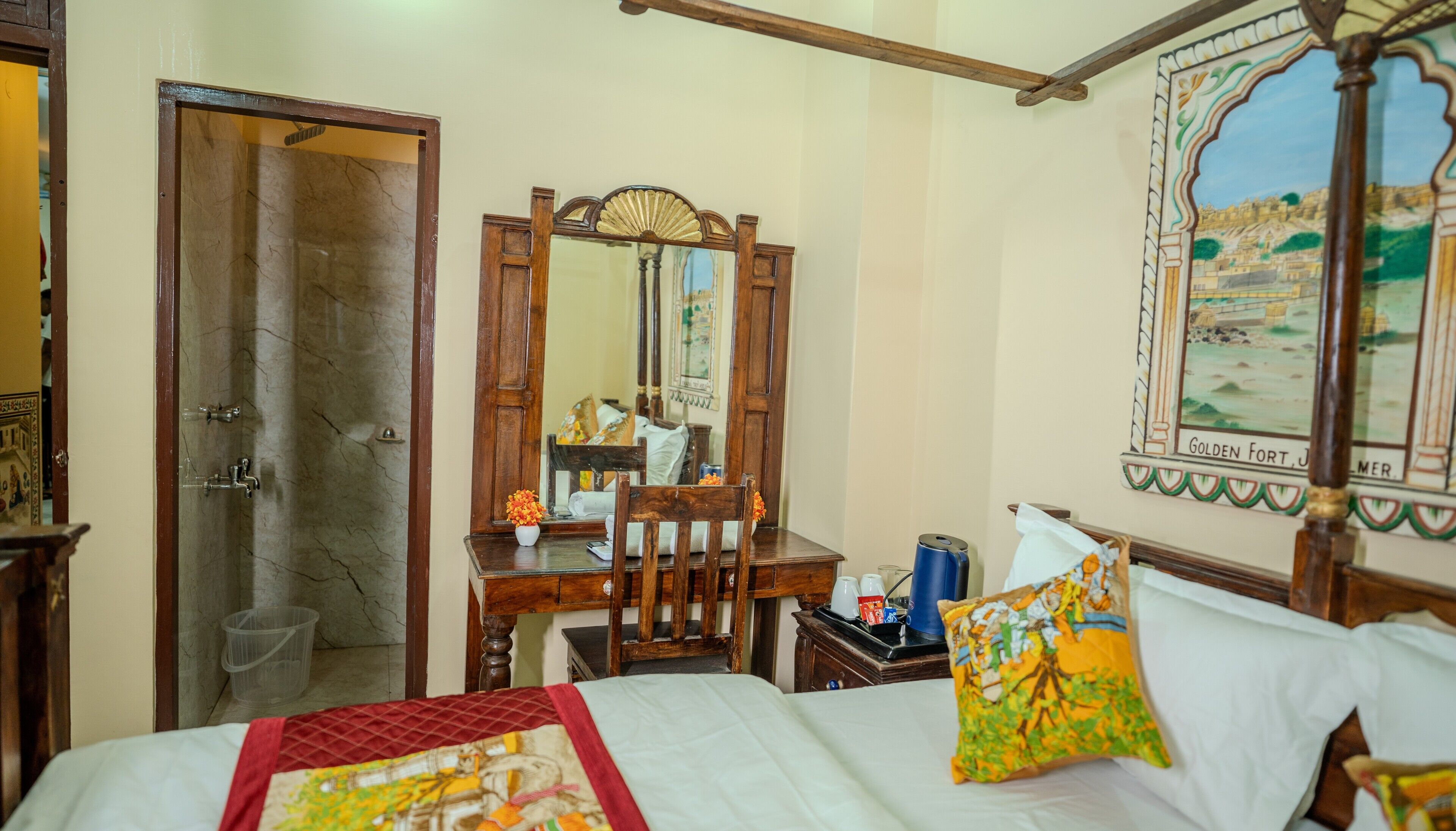 A hotel room with a bed, a wooden chair, a desk, a mirror, and a wall with a painting.