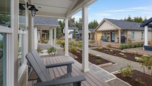 Ein überdachter Außenbereich mit einer hölzernen Bank, ein Garten mit erhöhten Blumenbeeten und Blick auf benachbarte Häuser.