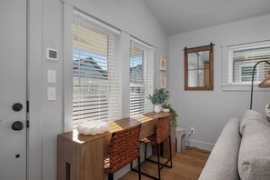 Una sala de estar moderna con una mesa consola de madera, dos taburetes, un sofá y un ventanal con persianas.