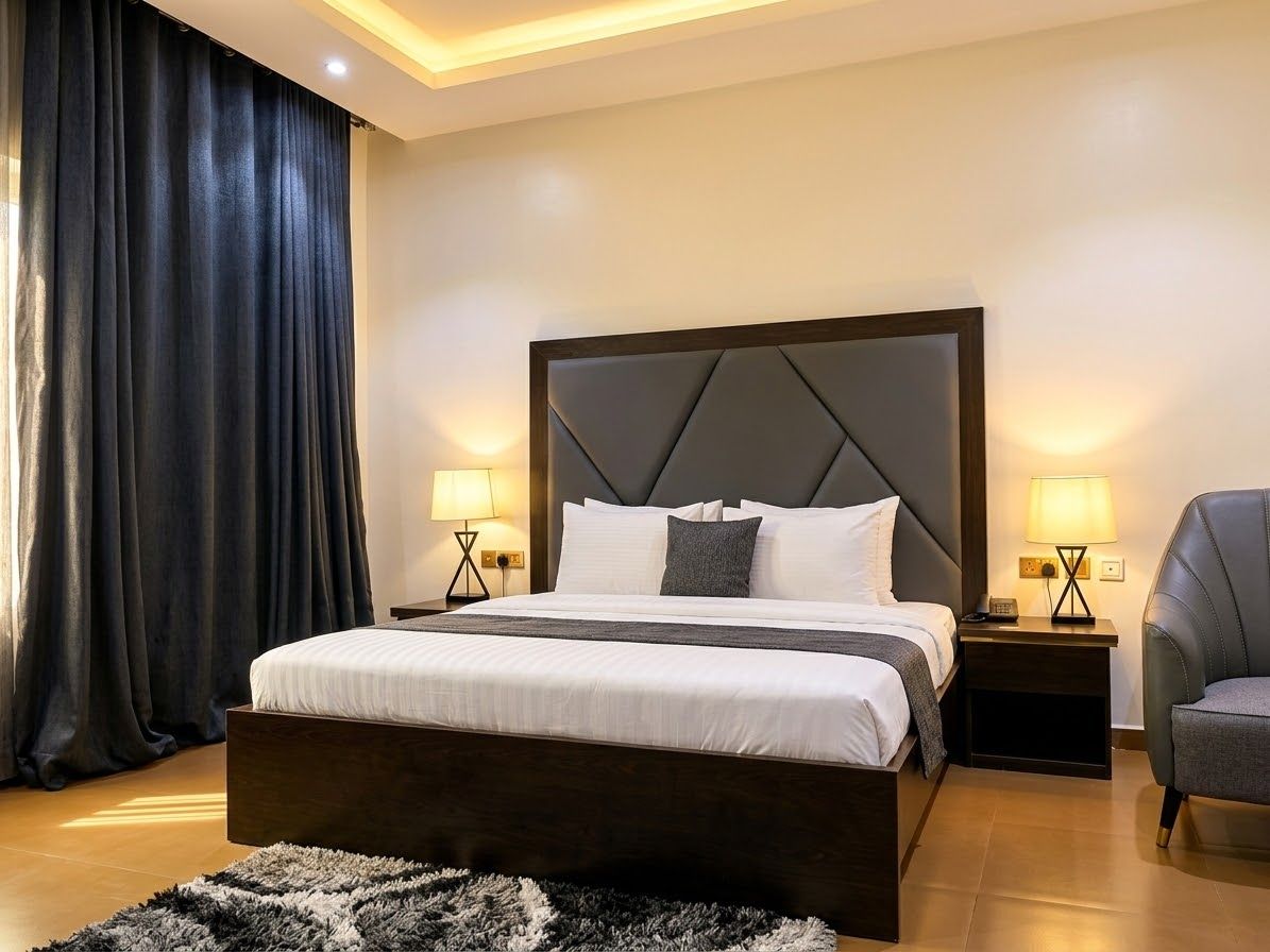 Una habitación de hotel moderna con una cama grande, dos mesitas de noche, una silla y una cortina oscura.
