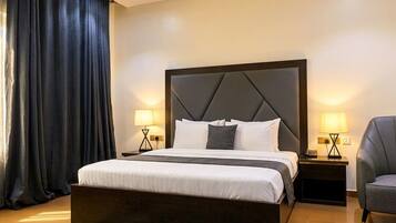 Una habitación de hotel moderna con una cama grande, dos mesitas de noche, una silla y una cortina oscura.