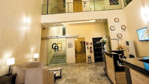 Un vestíbulo de hotel con mostrador de recepción, zona de estar y una escalera que conduce a un piso superior.