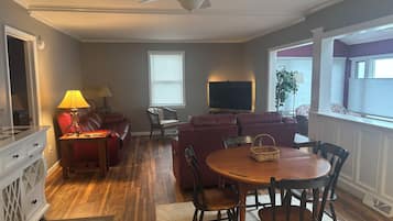 Ein Wohnzimmer mit einem roten Sofa, einem Holzesstisch mit Stühlen, einem Deckenventilator und einem Fernseher.