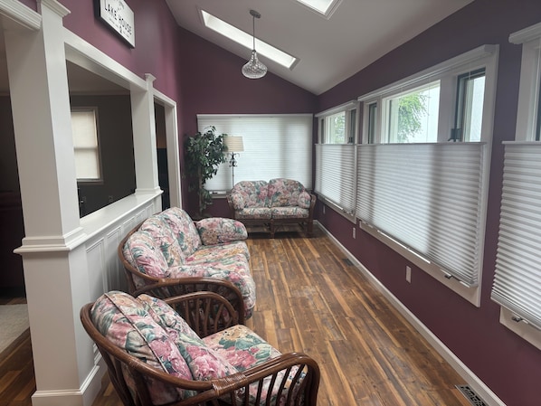 A room with a wooden floor, two wicker chairs with floral upholstery, a potted plant, and a ceiling light fixture.