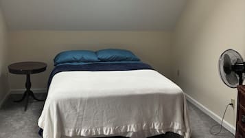 A bedroom with a single bed, a small round table, a standing fan, and a skylight.