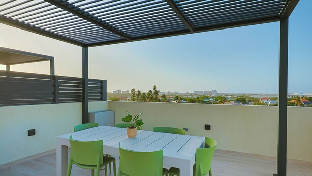 Un patio al aire libre con una mesa, sillas, una planta en maceta y vistas a un paisaje urbano.