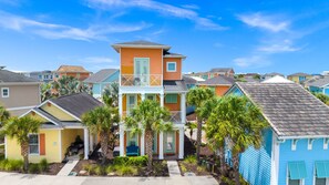 A residential area with colorful houses, a central two-story building with a balcony, and palm trees. - Tropical Cottage near Disney | Resort & Waterpark Access - 3095KL (Kissimmee)