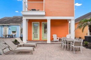 Un immeuble de deux étages doté d’un balcon, d’une terrasse avec mobilier d’extérieur et d’un bâtiment bleu situé à côté.