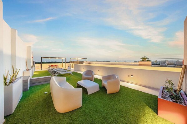 Une terrasse sur le toit, avec un revêtement d’herbe artificielle, des fauteuils blancs et une vue sur le panorama urbain.