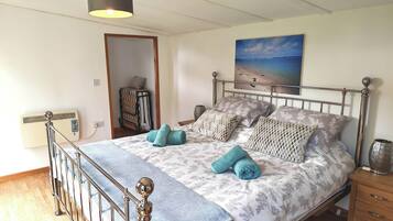 A bedroom with a metal-framed bed, a wall-mounted heater, a painting of a beach, and a wooden nightstand.