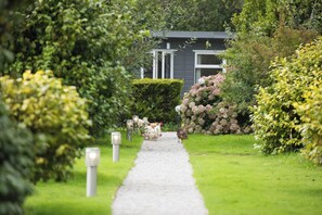 A pathway leading to a house surrounded by lush greenery and flowering plants. - Hazel Lodge (Falmouth)