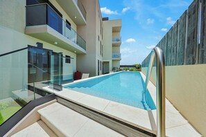 A modern residential building with a swimming pool, glass railings, and a clear sky. - Bonsai 1BR Suite-Maple 308 (Noord)