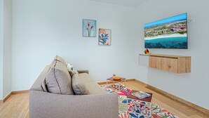 Uma sala de estar com um sofá, uma televisão de tela plana na parede e duas obras de arte emolduradas.