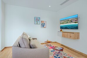 A living room with a sofa, a flat-screen TV mounted on the wall, and two framed artworks. - Bonsai 1BR Suite-Wood Heaven 305 (Noord)