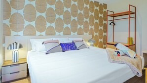 Quarto de hotel com uma cama grande, mesa de cabeceira, luminária pendente e guarda-roupa com espelho.