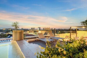A rooftop terrace with lounge chairs, a small pool, and a city view at dusk. - Bonsai Accessible 1BR Suite-Forest 111 (Noord)