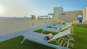 Eine Dachterrasse mit Liegestühlen, einem kleinen Pool und Blick auf das Meer.