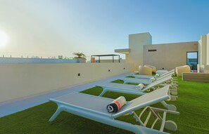 Eine Dachterrasse mit Liegestühlen, einem kleinen Pool und Blick auf das Meer.