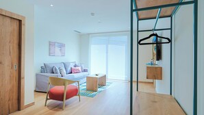 Ein modernes Wohnzimmer mit einer Couch, einem roten Sessel, einem Holztisch und einer Kleiderstange.