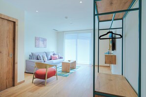 Ein modernes Wohnzimmer mit einer Couch, einem roten Sessel, einem Holztisch und einer Kleiderstange.