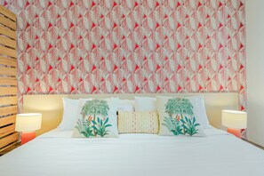 Un dormitorio con papel tapiz estampado, una cama con ropa de cama blanca y dos lámparas de noche.