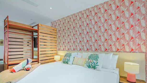 A bedroom with a bed, pillows, a nightstand, a lamp, and a wooden wardrobe. - Bonsai Studio-Bliss 304 (Noord)