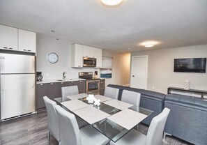 A modern kitchen with a dining area, including a glass table with chairs, a clock, and built-in appliances.