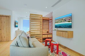 A modern living room with a sofa, a TV, a wooden partition, and a view of a coastal city. - Bonsai Studio-Blossom 303 (Noord)