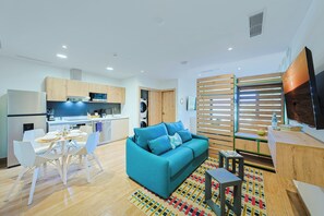 Ein modernes Wohnzimmer mit einer Couch, einem Essbereich mit Stühlen, einer Küche mit Geräten und einem Fernseher an der Wand.