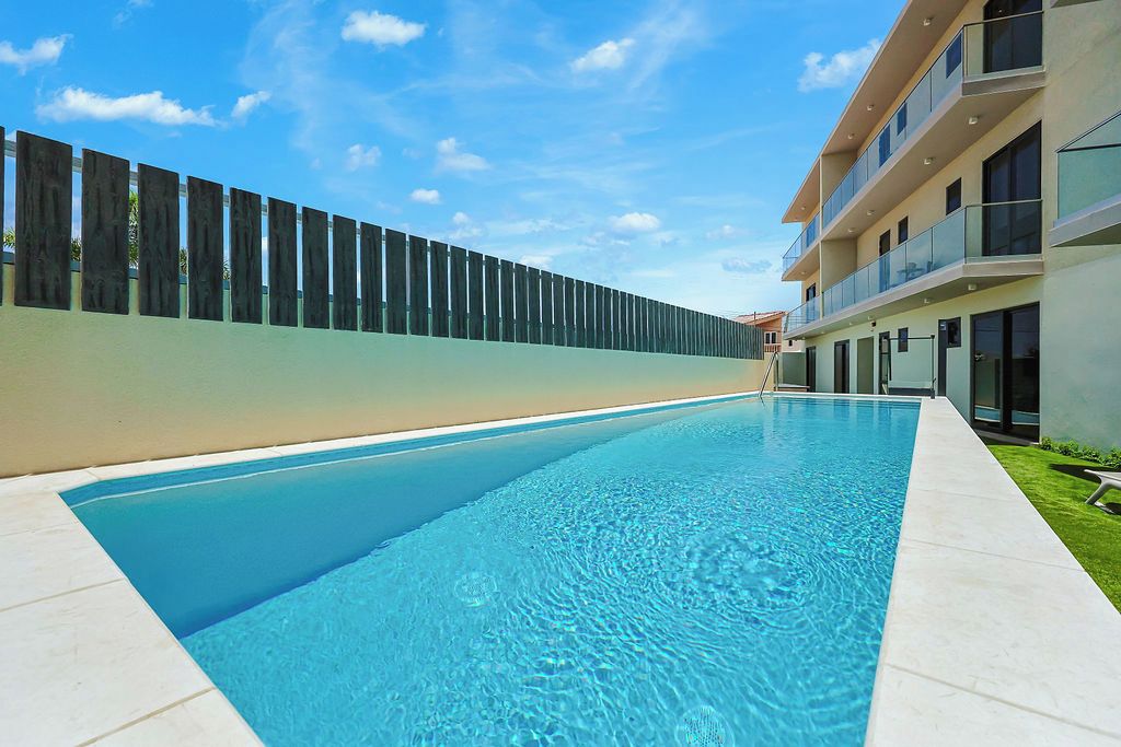 Ein Schwimmbecken mit modernem Design, umgeben von einer niedrigen Mauer und einem Gebäude mit Balkonen.