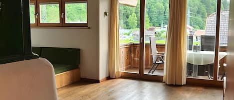 A spacious room with wooden floors, a ceiling fan, and large windows with curtains.