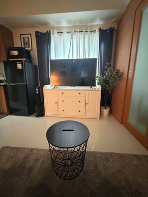 Ein Wohnzimmer mit Fernseher, Schrank, kleinem Tisch und einer Zimmerpflanze.