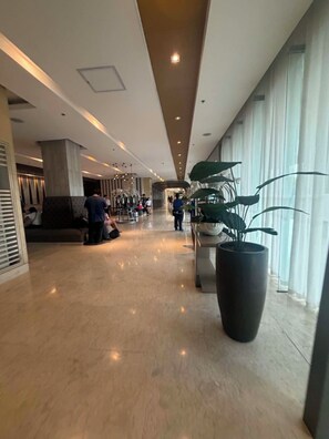 Eine geräumige Lobby mit hoher Decke, großen Kübelpflanzen und einer Sitzecke mit Personen.