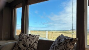 A room with a sofa facing large windows with a view of a rural landscape. - Bwlchgwyn Caravan, Aberdaron (Pwllheli)