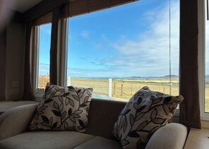 Ein Zimmer mit einer Couch, die zu großen Fenstern mit Blick auf eine ländliche Landschaft hinweist.