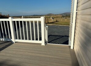 A wooden deck with a white railing, a clear view of a fenced pasture with cows, and a distant landscape. - Bwlchgwyn Caravan, Aberdaron (Pwllheli)