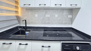 A kitchen with a black induction cooktop, white cabinets, and a marble backsplash. - Lovely 1-Bedroom in Victoria Island with Pool, Fast Wi-Fi & 24/7 Power (Lagos)