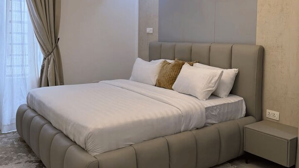 A modern bedroom with a large bed, a bedside table, and a unique ceiling light fixture. - Lovely 1-Bedroom in Victoria Island with Pool, Fast Wi-Fi & 24/7 Power (Lagos)
