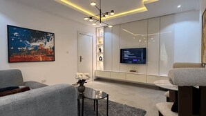A modern living room with a grey sofa, a coffee table, and a TV mounted on the wall. - Lovely 1-Bedroom in Victoria Island with Pool, Fast Wi-Fi & 24/7 Power (Lagos)