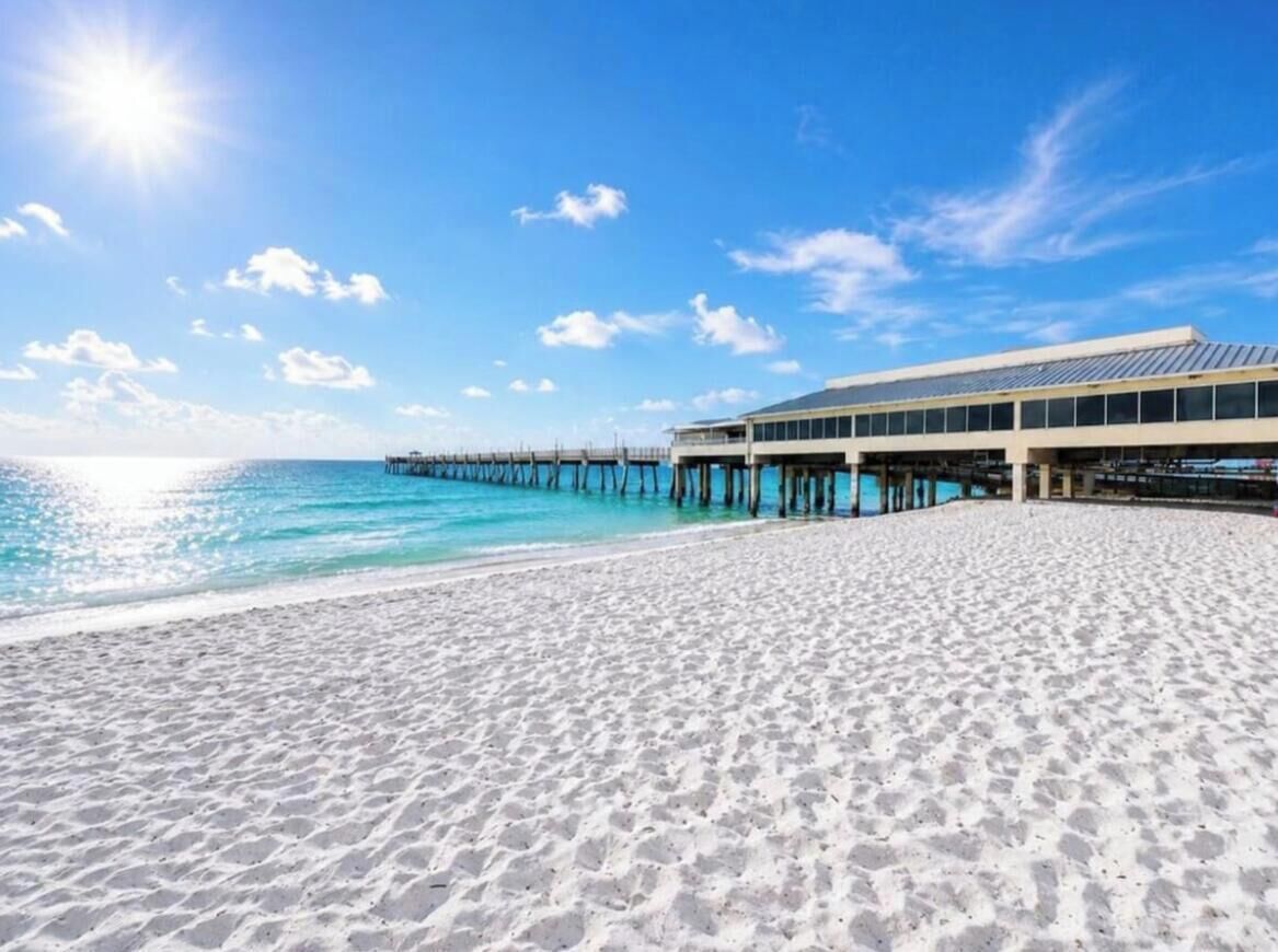 A beach with a pier extending into the water, a building adjacent to the beach, and clear skies.