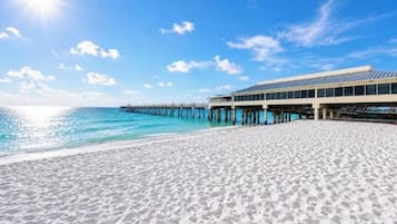 A beach with a pier extending into the water, a building adjacent to the beach, and clear skies.