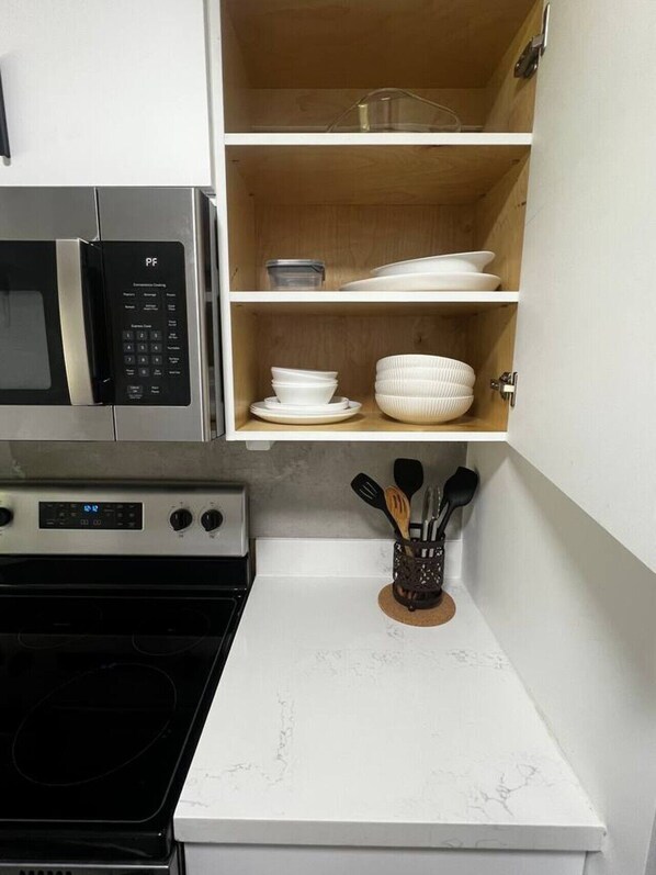 A kitchen with a microwave, oven, and a cabinet with dishes and utensils.