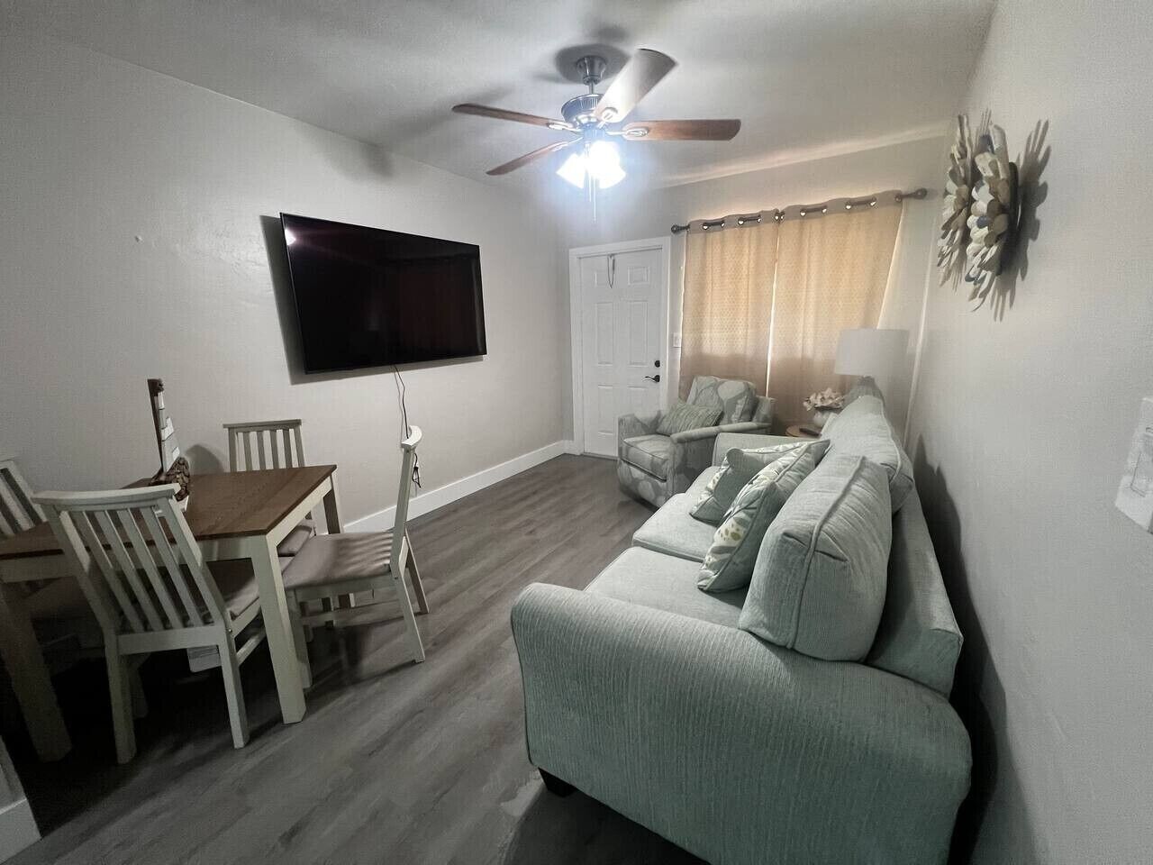 A living room with a flat-screen TV, ceiling fan, dining table with chairs, and a sofa.