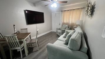 A living room with a flat-screen TV, ceiling fan, dining table with chairs, and a sofa.