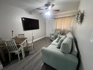 A living room with a flat-screen TV, ceiling fan, dining table with chairs, and a sofa.