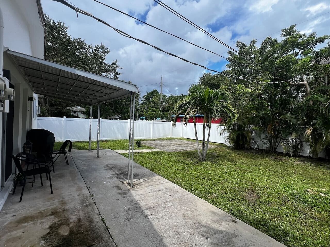 Un patio cubierto con muebles de exterior, cerca blanca y césped.